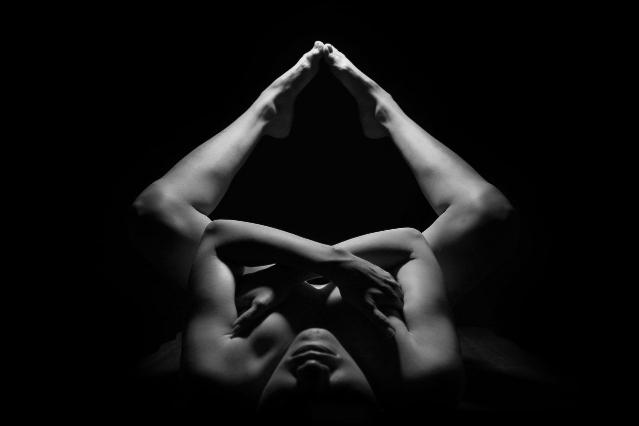 Black and white photograph showcasing an artistic nude pose with dramatic lighting and shadows.
